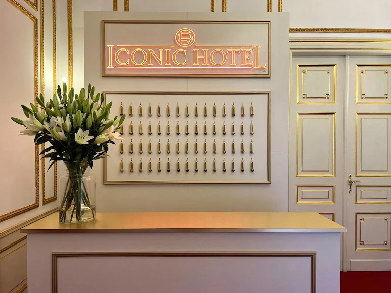 Weiß-pinkes „Iconic Hotel“-Leuchtschild hinter einer Rezeption